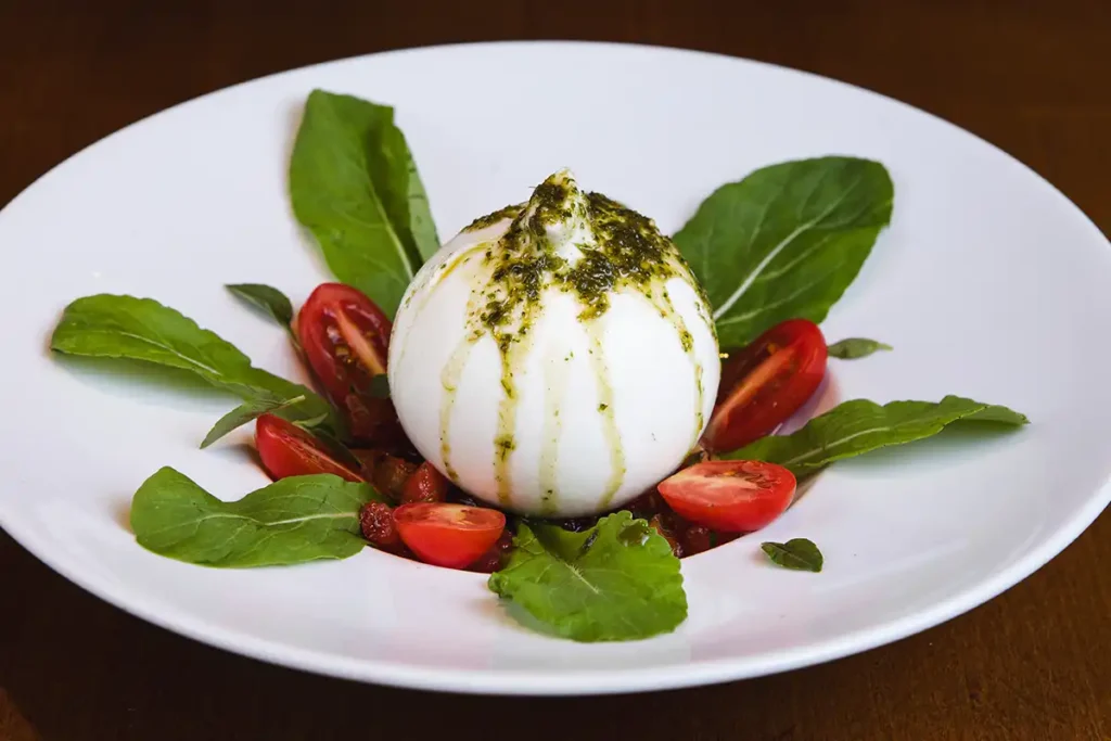 Burrata - queijo de búfala, servido ao molho pesto, tomate cereja, manjericão, rúcula e torradas